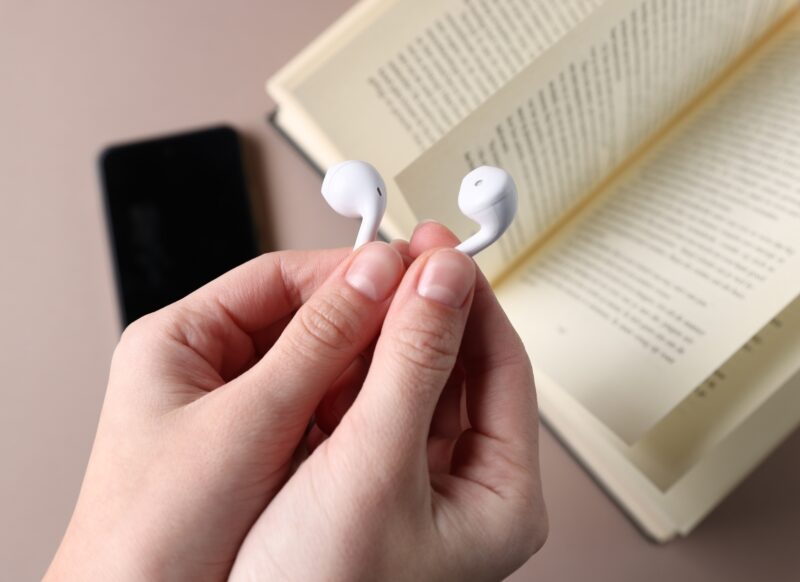 prikaz slušalica kod osobe u ruci i u pozadini knjiga i telefon