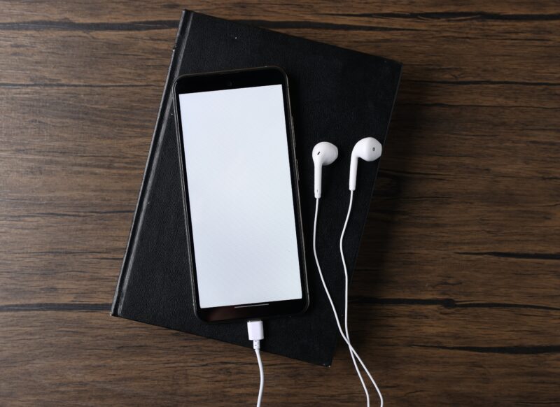 prikaz audio knjige na telefonu, slušalica i knjige obične