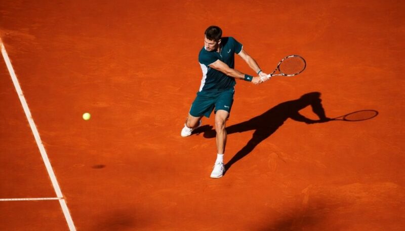Teniser izvodi udarac na šljaci tokom meča na otvorenom terenu